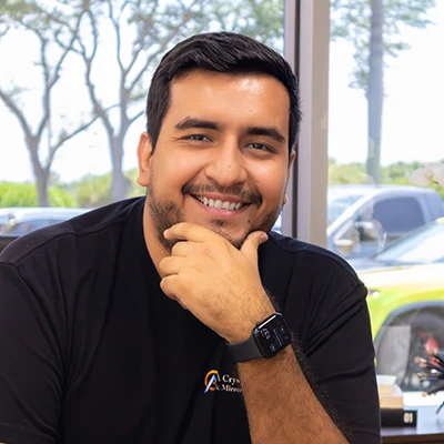 Close-up of a smiling man in a Crystal Glass & Mirror uniform indoors, with windows and trees in the background.