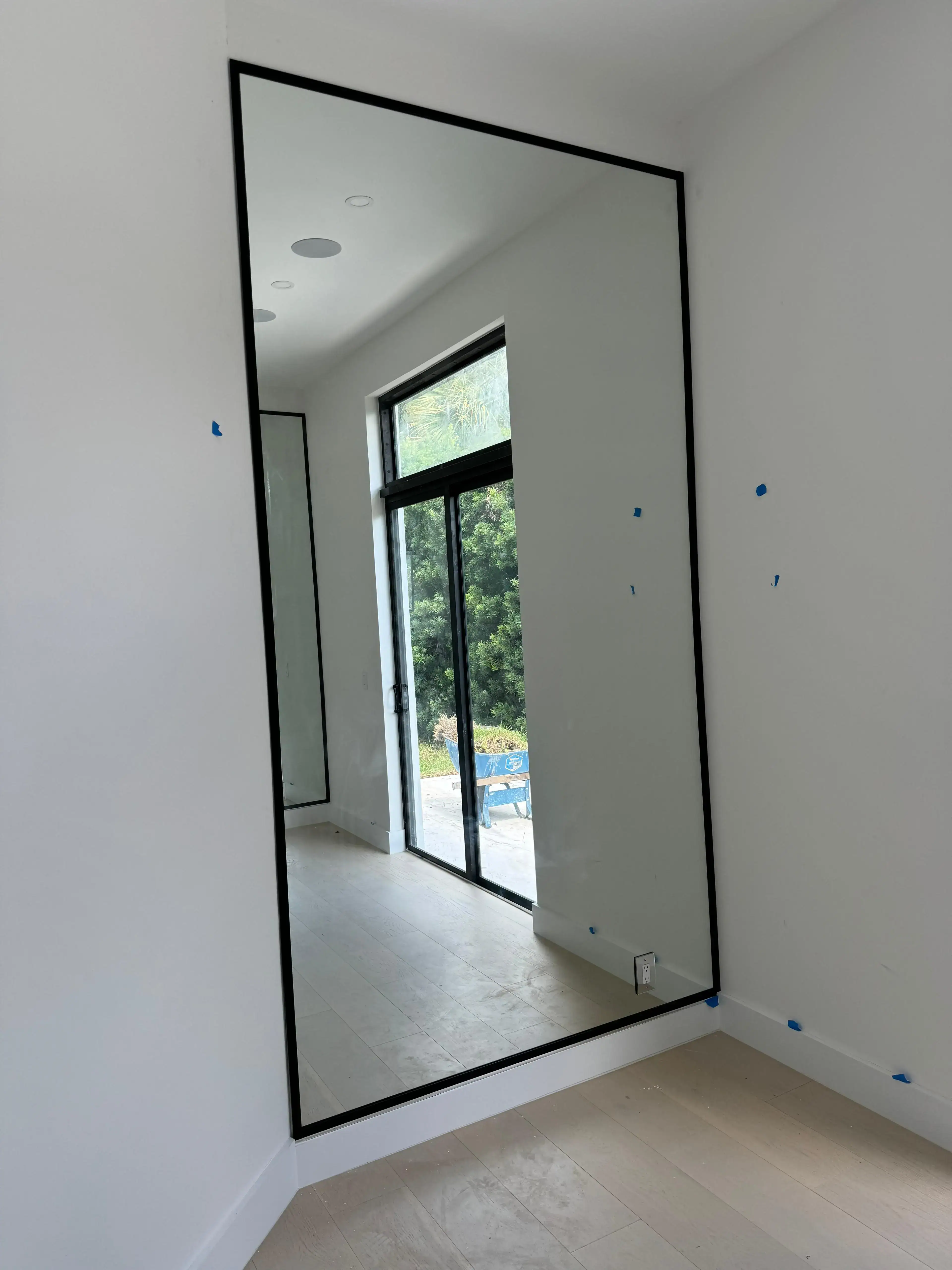 Large wall mirror reflecting natural light and outdoor scenery in contemporary living space.