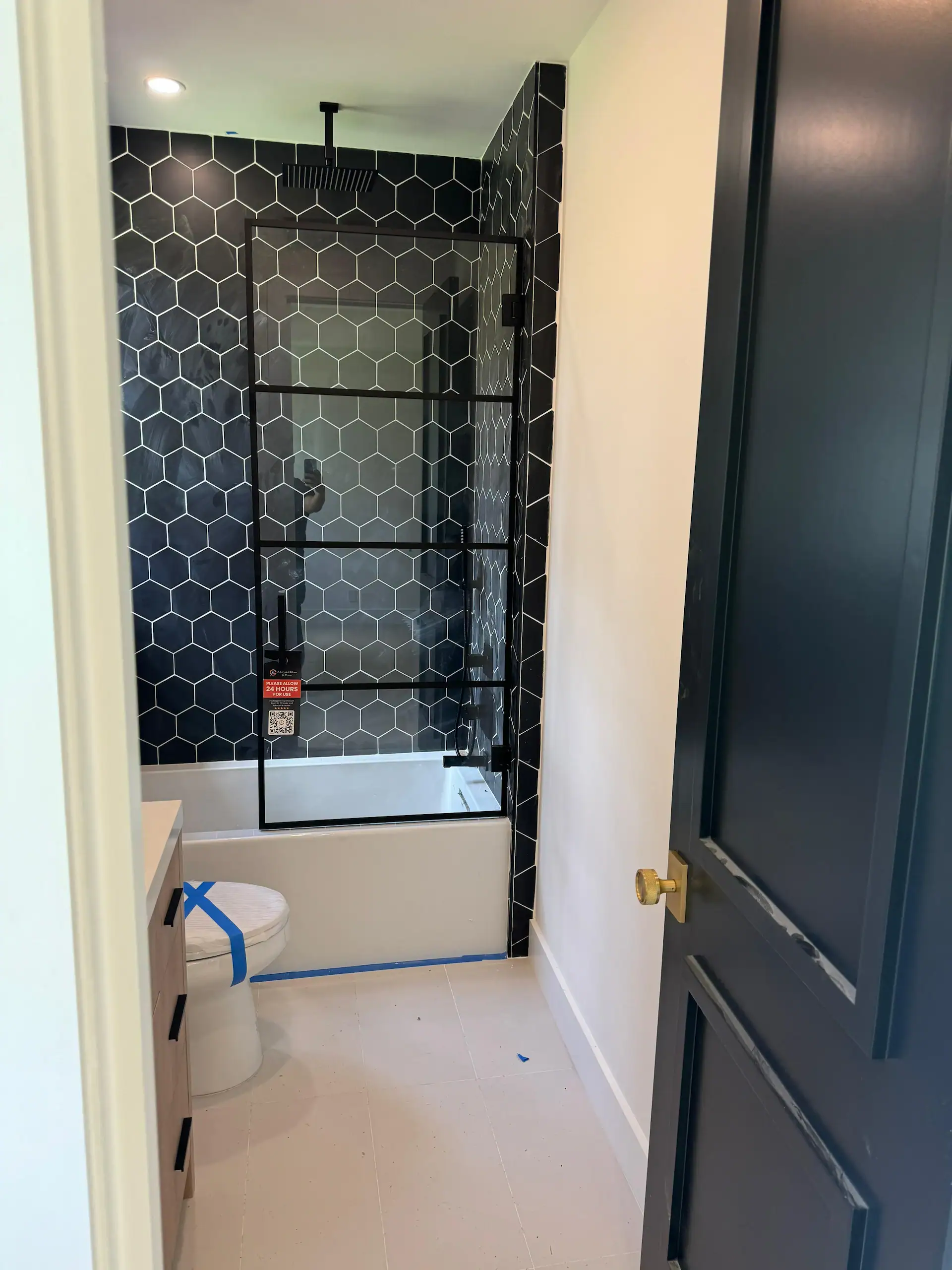Custom glass shower door with black hex tile accents, sleek bathroom design, high-quality glass.
