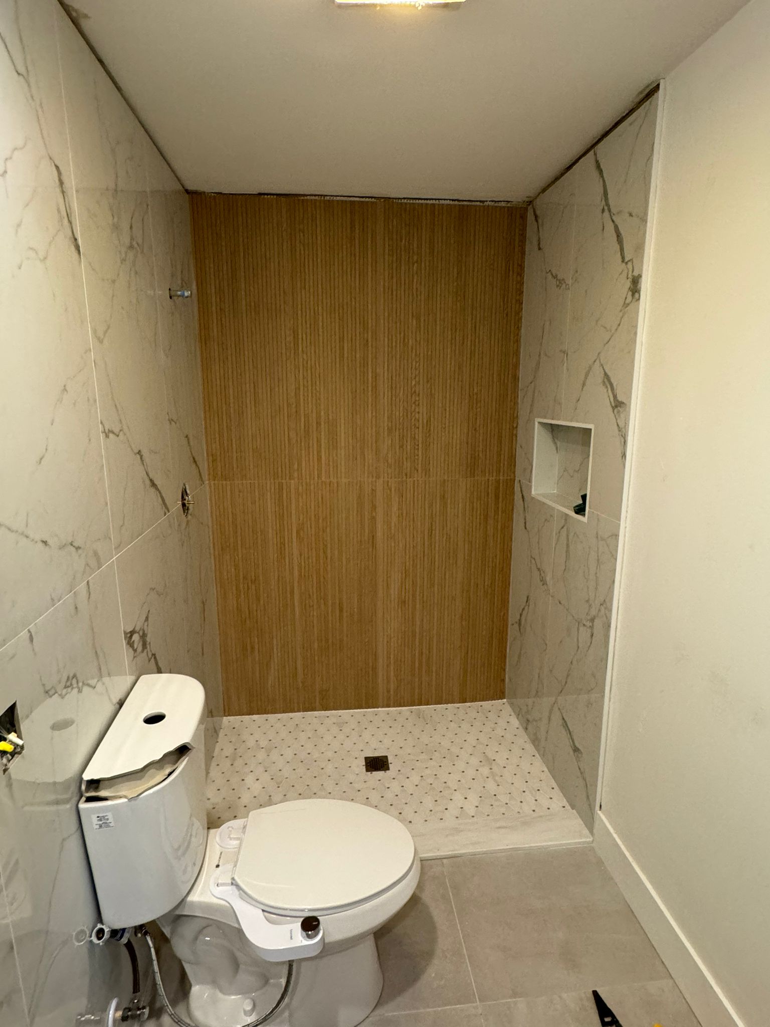 Bright modern bathroom with marble walls and wooden accent wall.