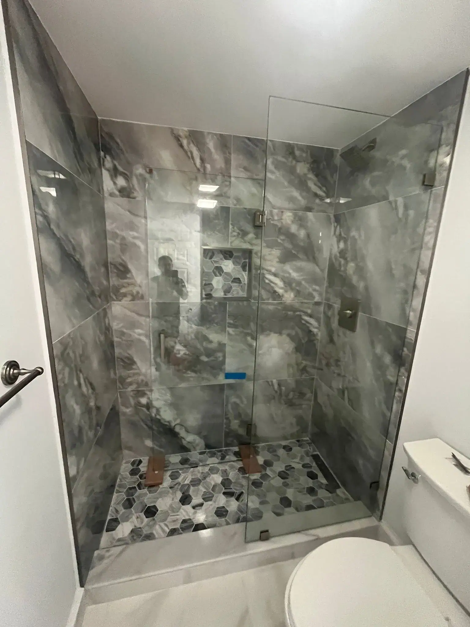 Reflective Glass Shower Door with Marble Tiles.