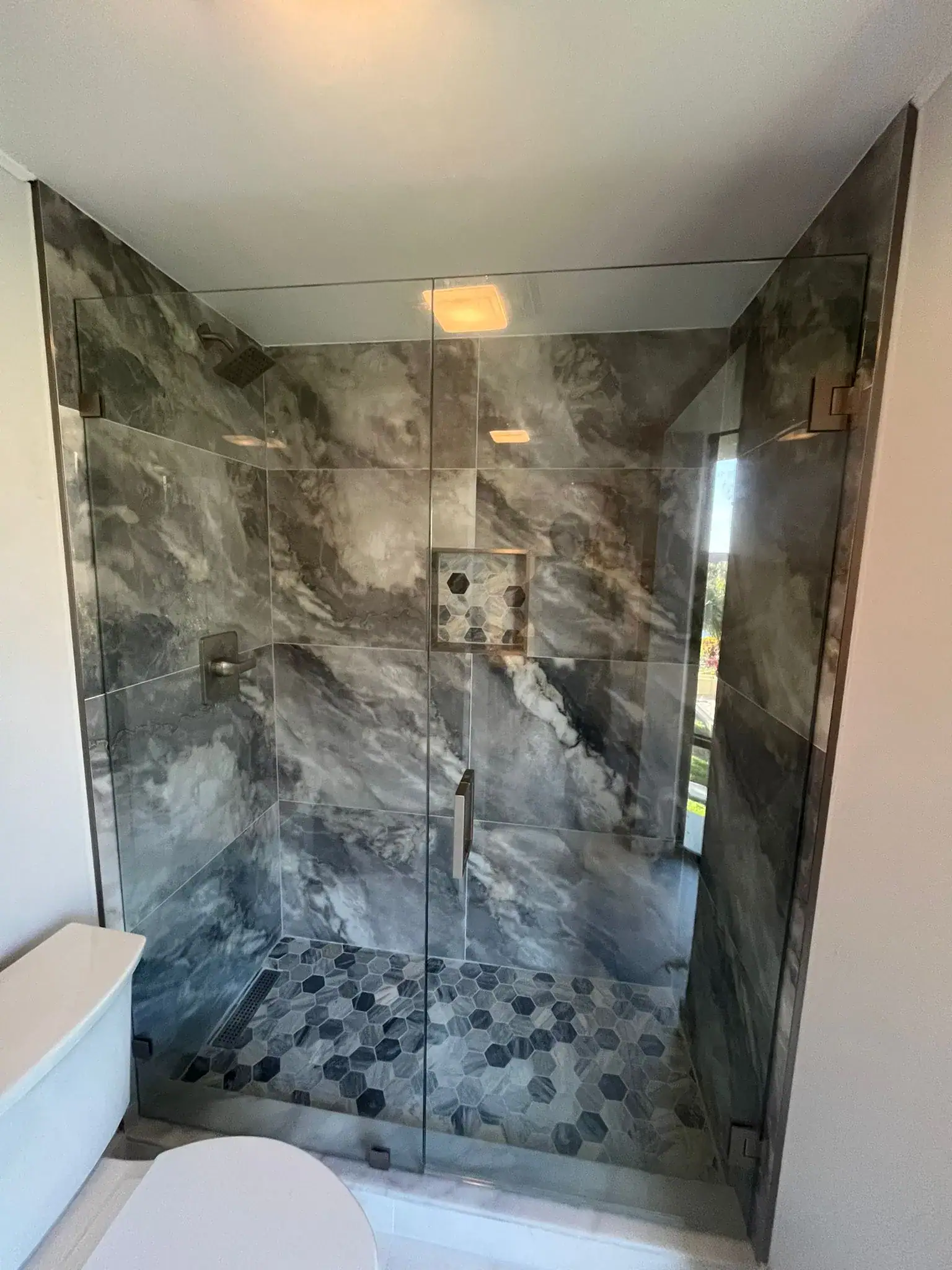 High-end glass shower enclosure with marble walls and hexagon floor tiles. Modern design, durable glass, and elegant finish.