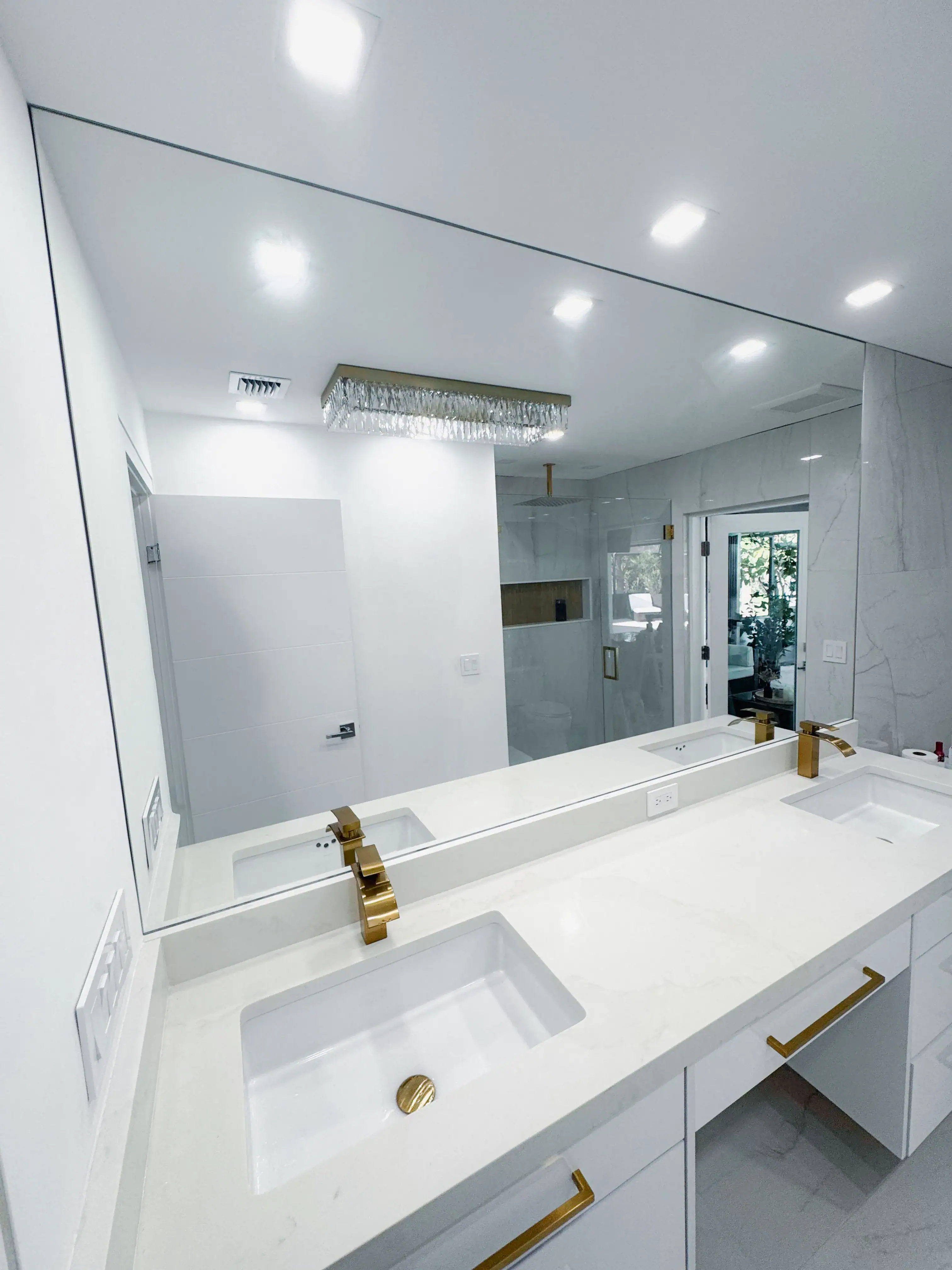 Alt text: Modern bathroom mirror with double sinks and gold fixtures in a bright, white space.
