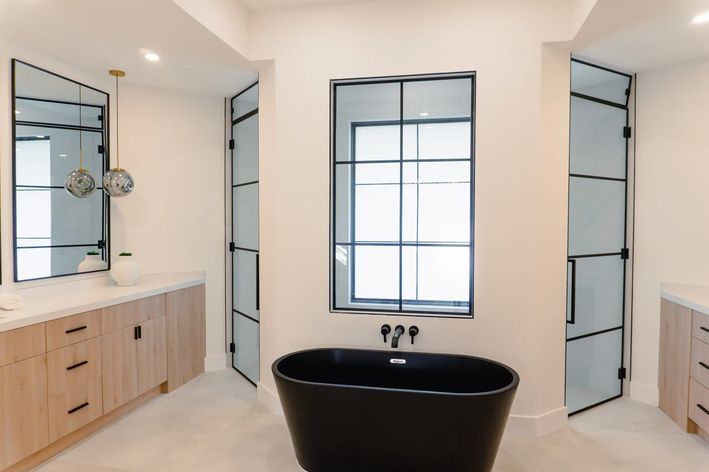 Luxury bathroom showcasing custom glass shower enclosures and a striking black bathtub. Modern design and sleek finishes.