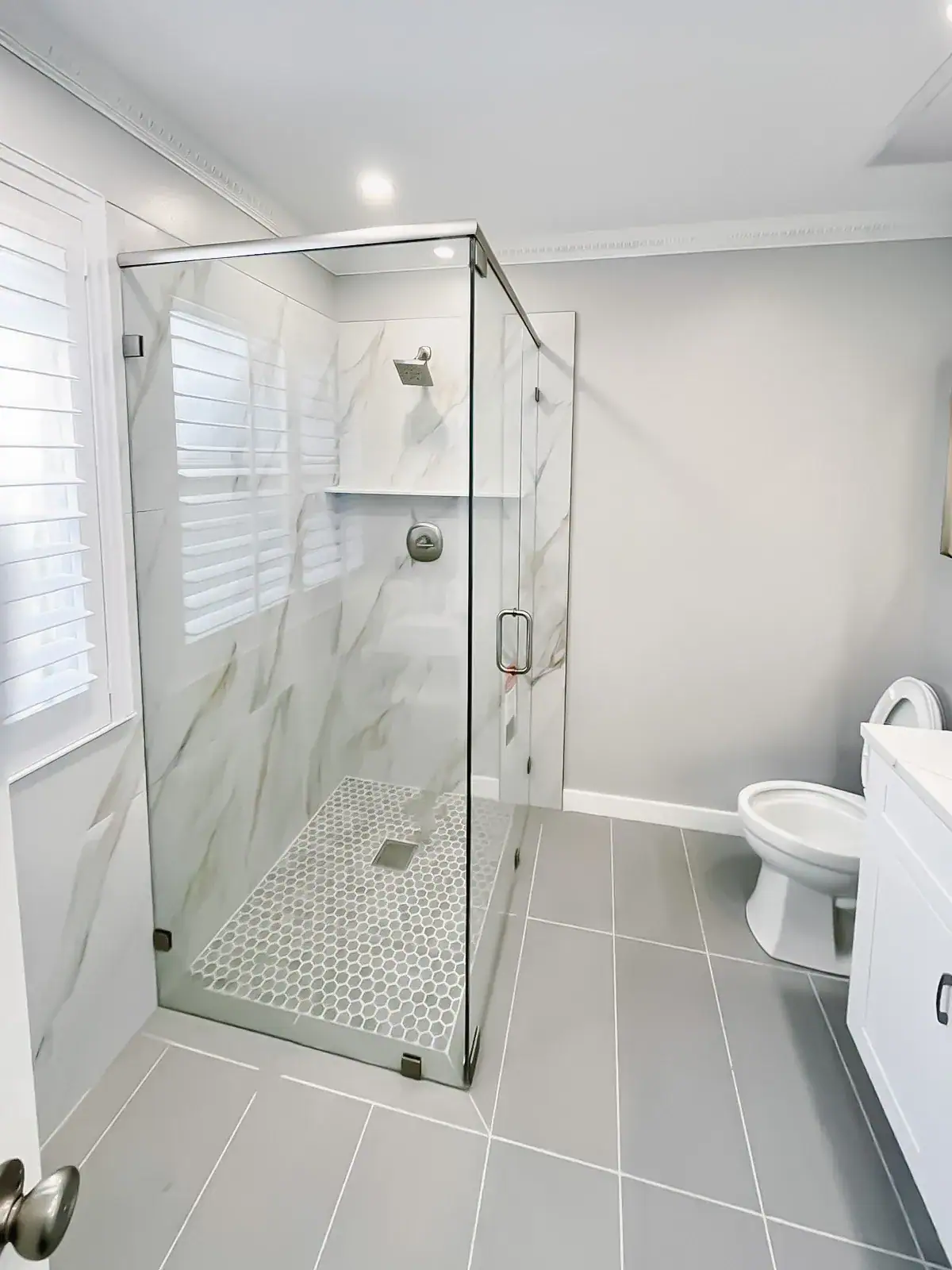 Alt text: Modern glass shower with marble tile, sleek metal handle, and minimalist design.