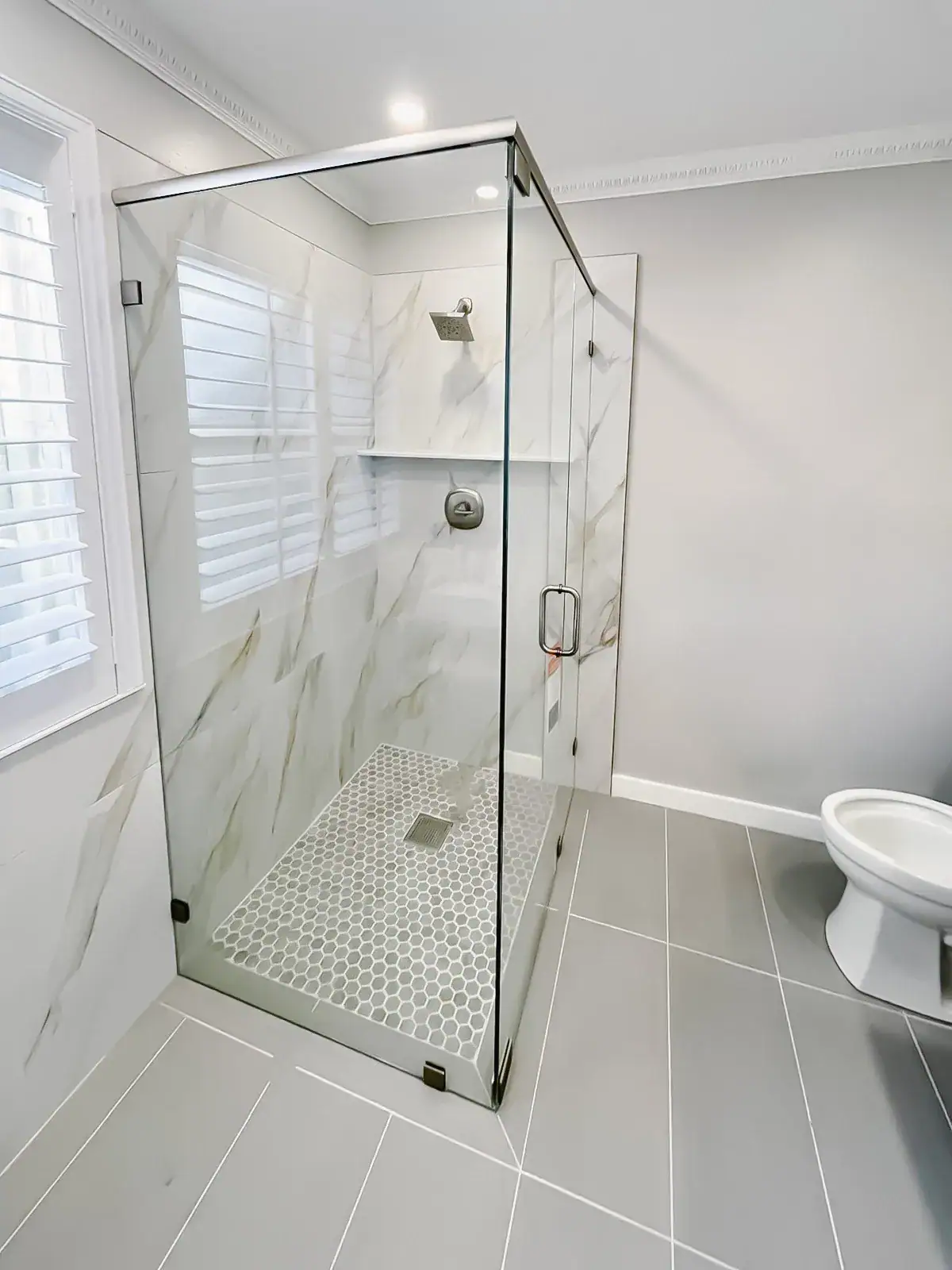 High-quality glass shower door with sleek stainless steel framing, marble walls, and updated bathroom fixtures.