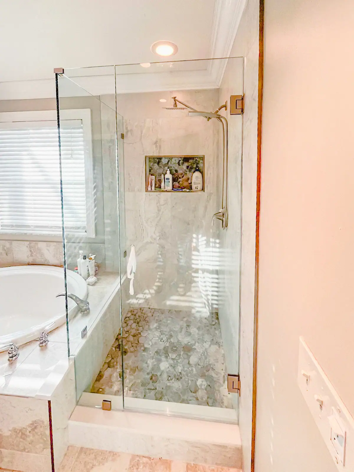 High-quality glass shower door with clear view, modern bathroom design featuring a marble tub and pebble tile floor.