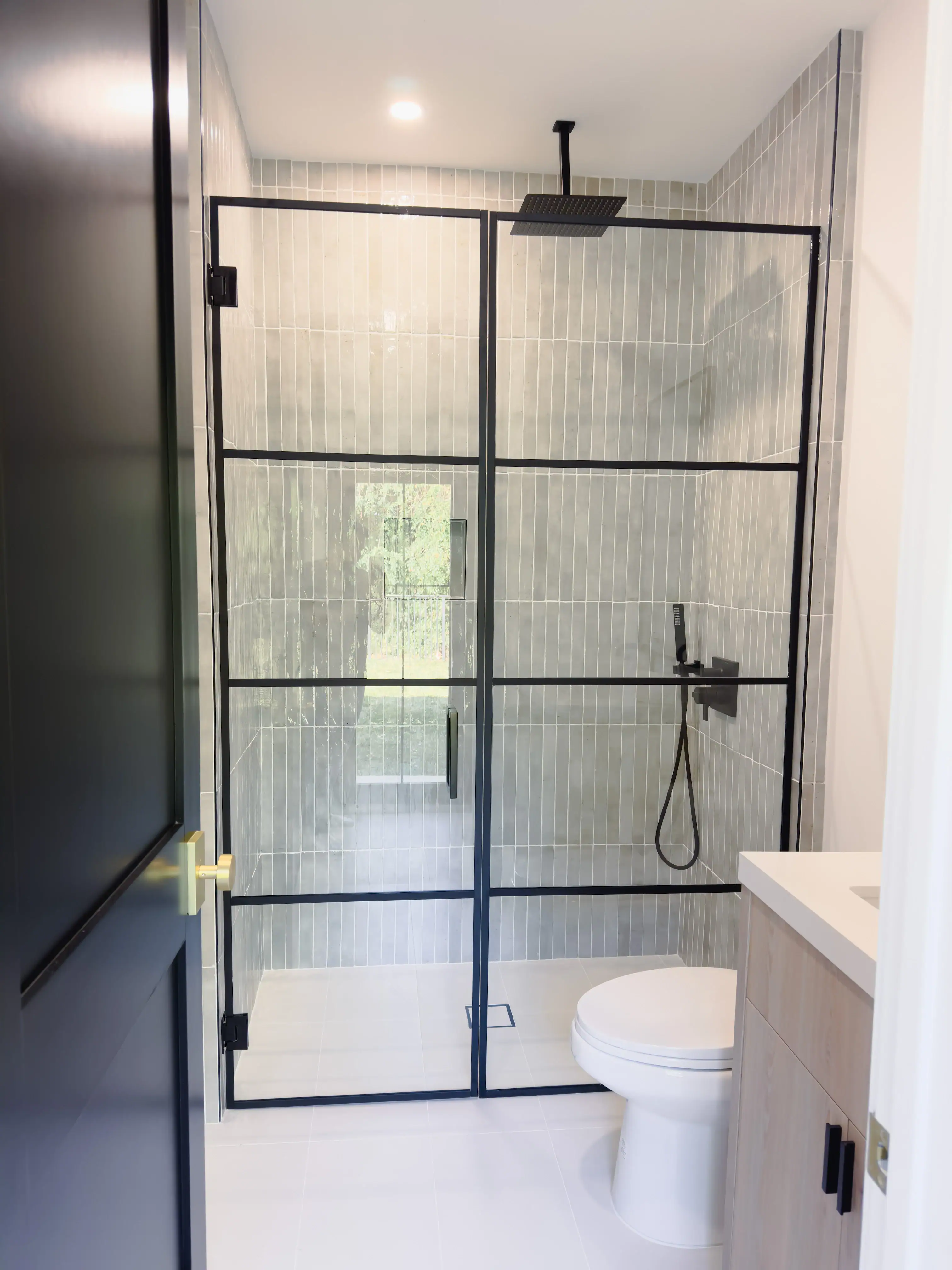 Glass shower door with black metal framing in contemporary bathroom.
