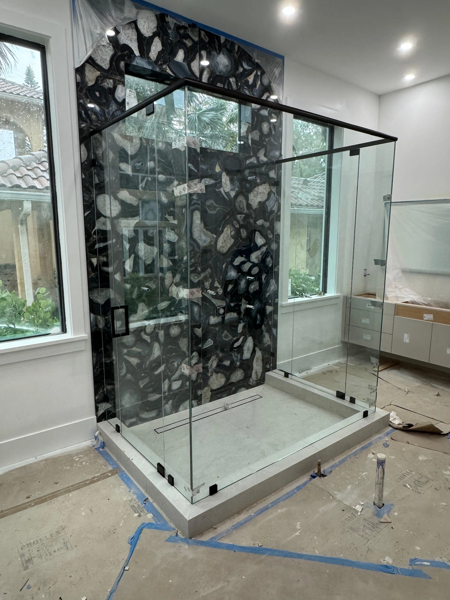 Clear glass shower stall with black hardware, featuring a stylish backdrop of black and gray stones.