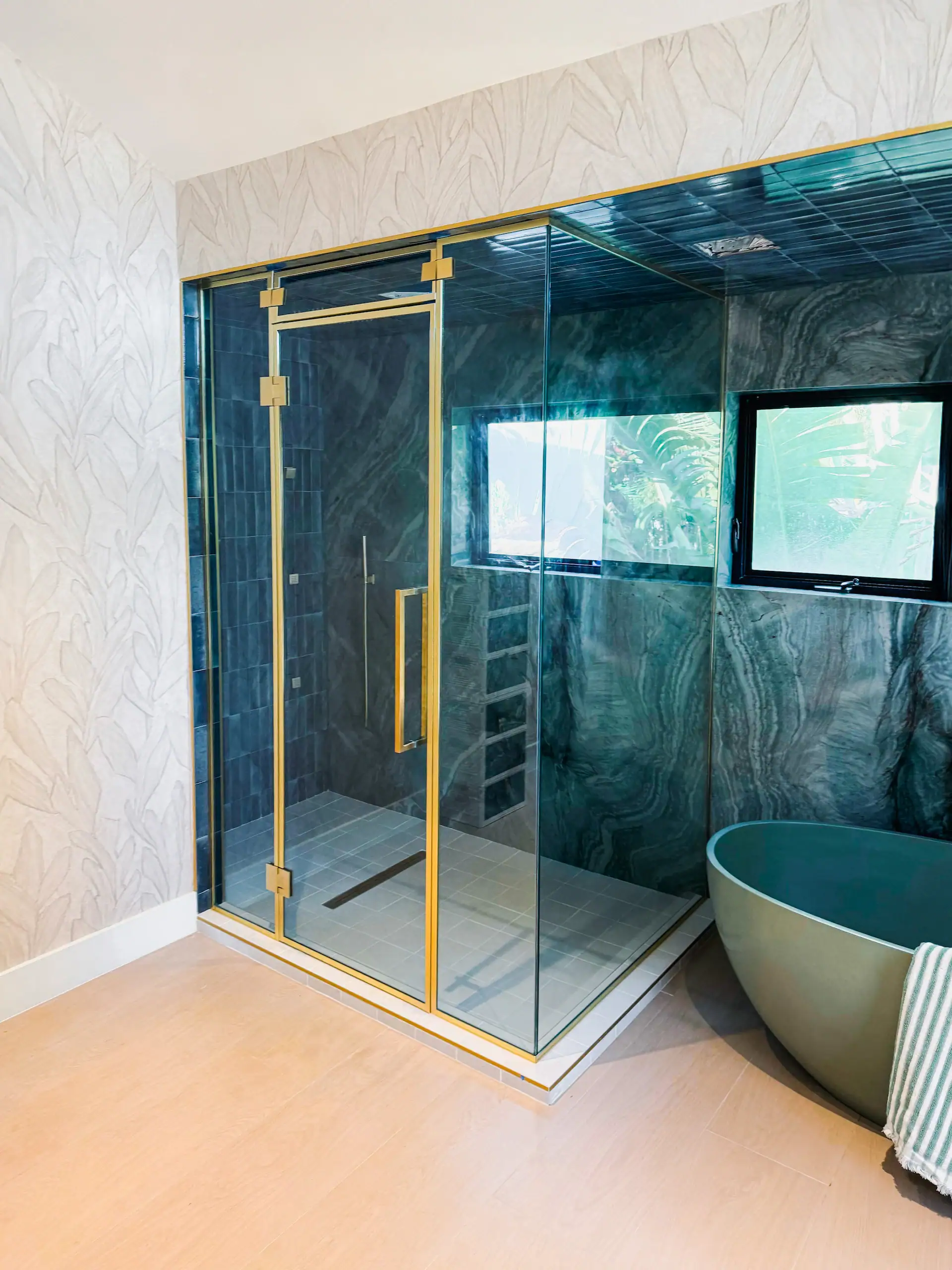 Clean, modern glass shower with gold framing and marble walls for luxury bathroom design.